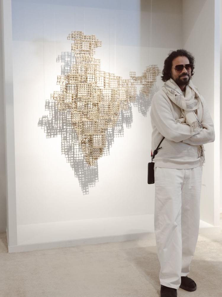 The designer Rahul Mishra in all white in front of a work by Ashiesh Shah