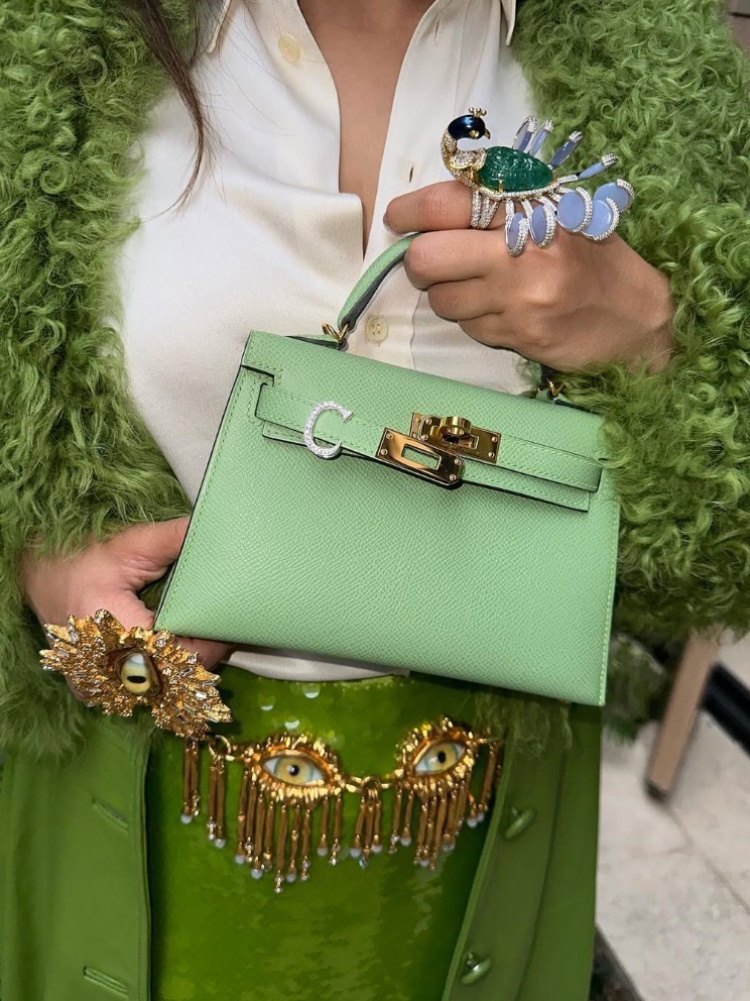 Ashna Mehta holding a green Hermès Kelly bag with a diamond initial charm by AM