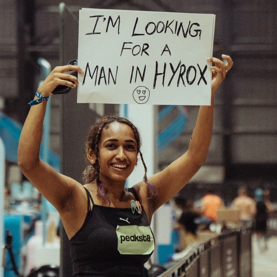 A woman at Hyrox, holding up a sign that reads: I'm looking for a man in Hyrox