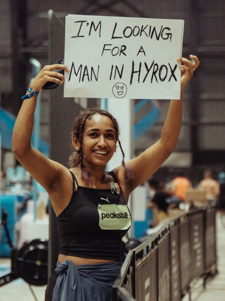A woman at Hyrox, holding up a sign that reads: I'm looking for a man in Hyrox