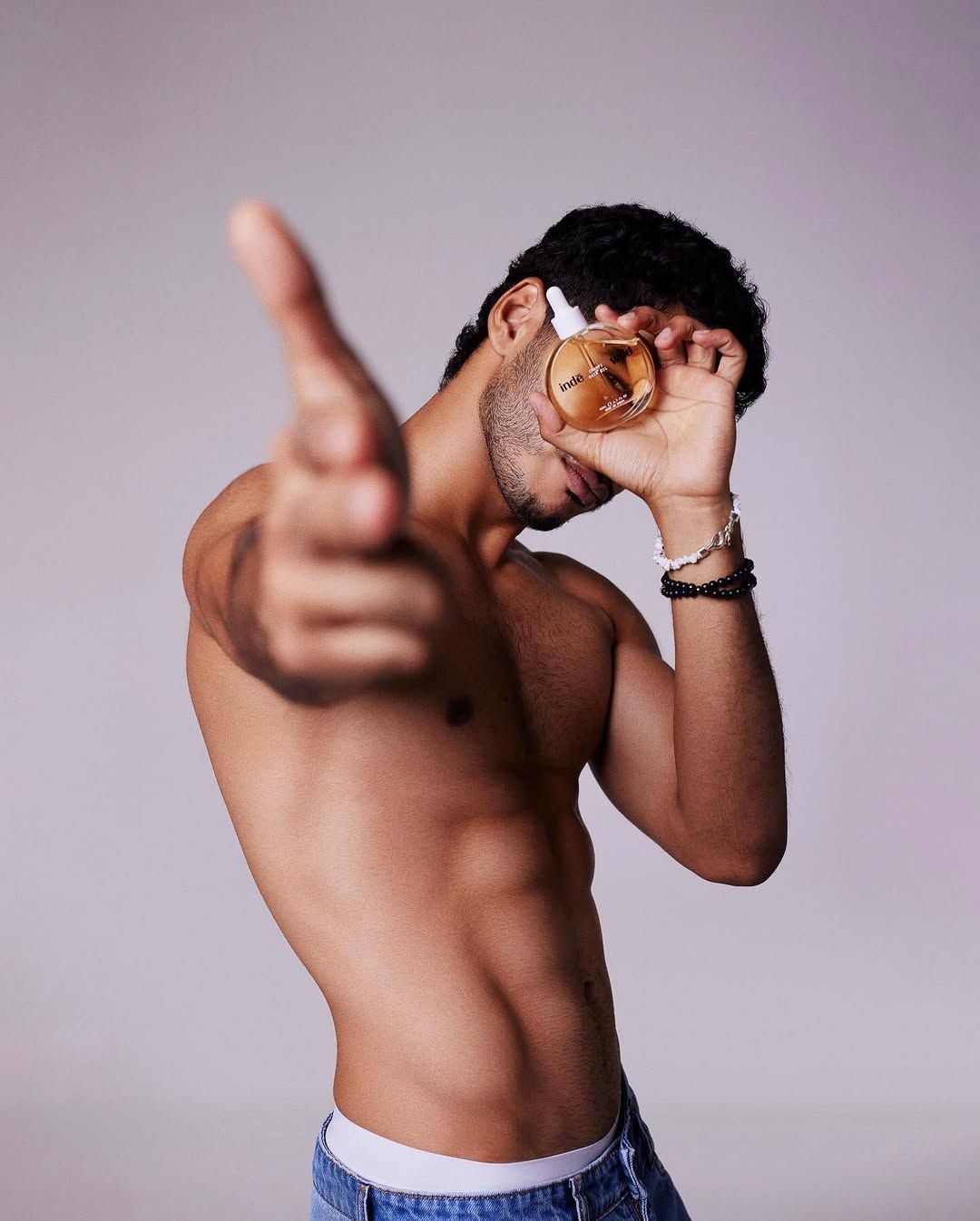 A shirtless Ishaan Khatter holding up a bottle of Inde Wild champi oil