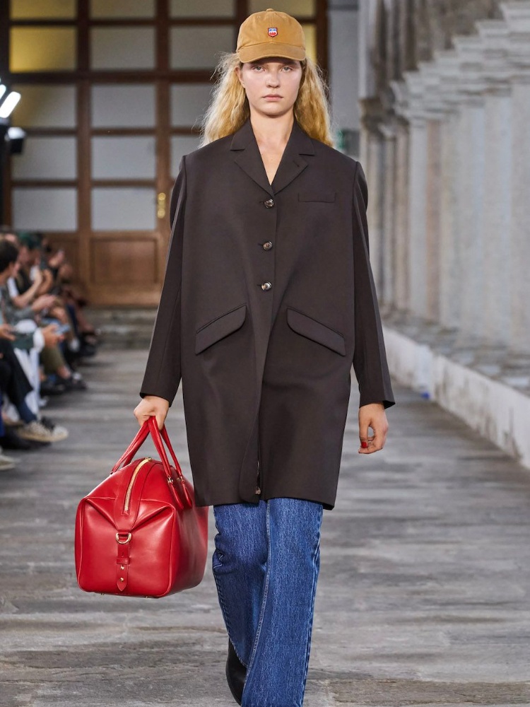 A model from the Bally spring/summer 2024 runway wearing a brown coat, red bag, and blue jeans