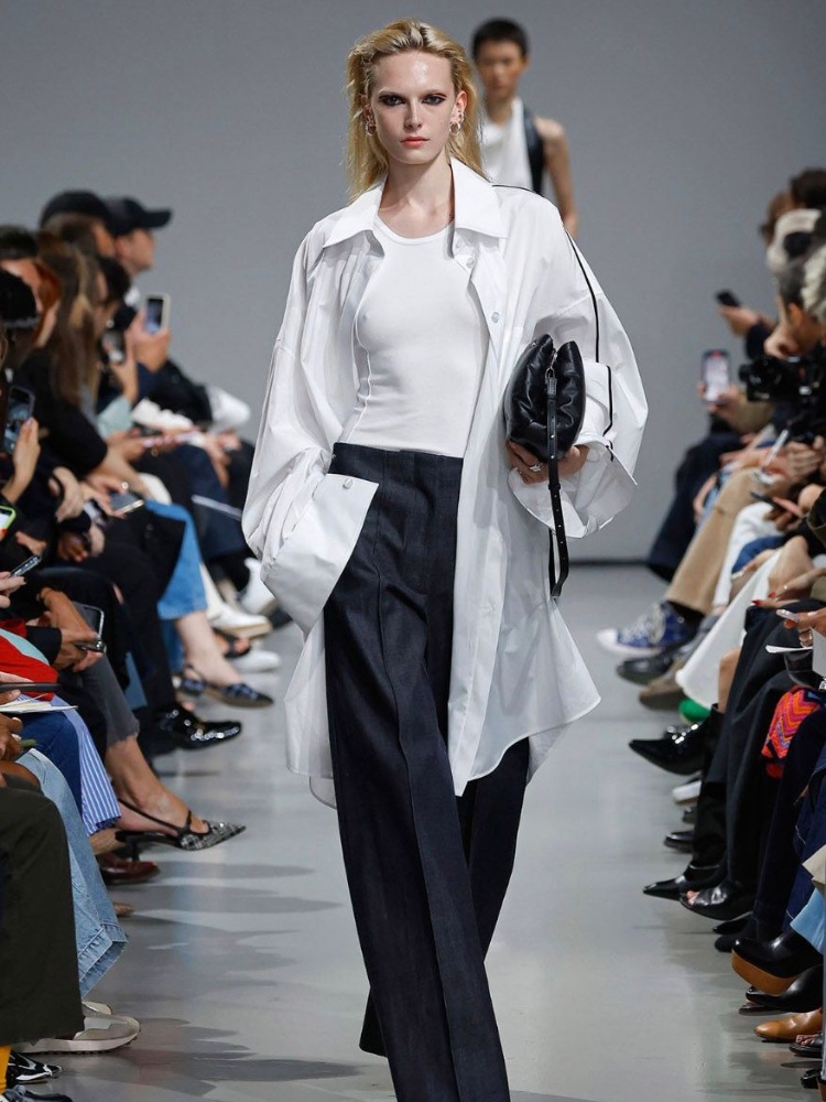 A still from the Peter Do spring/summer 24 runway featuring a model wearing a white t-shirt, an oversized white shirt and grey trousers