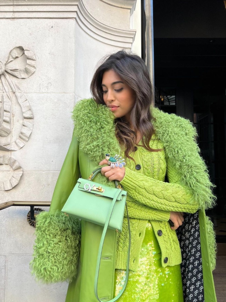 Ashna Mehta in an all-green outfit holding a green Hermès Kelly bag with a diamond initial charm by AM