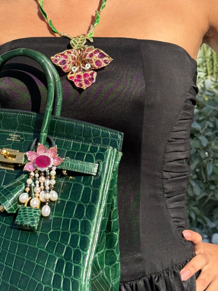 A woman holding a green Birkin bag accessorised with floral jewellery