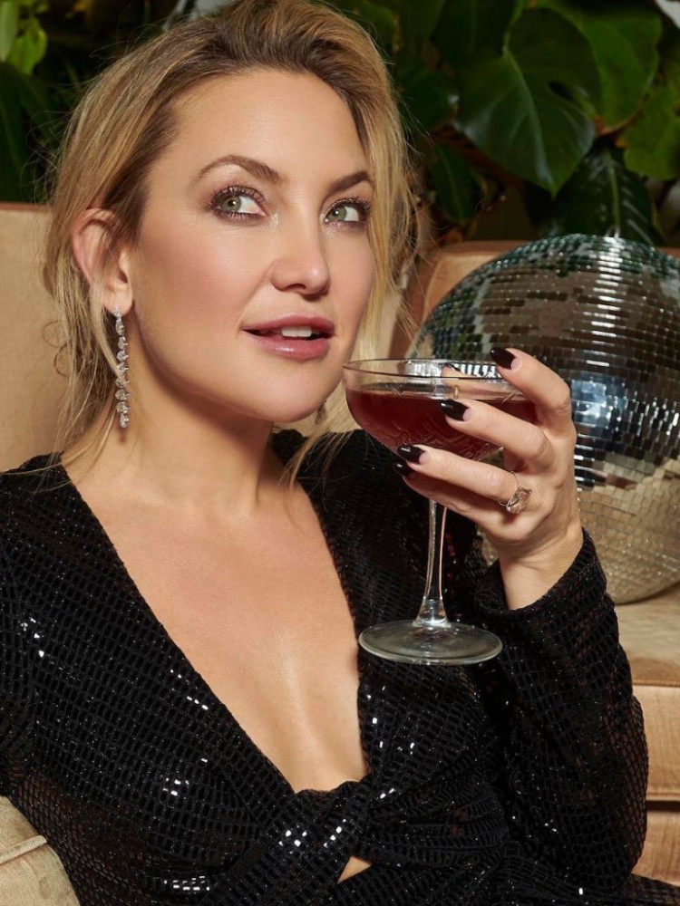 Kate Hudson in a black dress holding a drink, wearing her east-west Lorraine Schwartz engagement ring