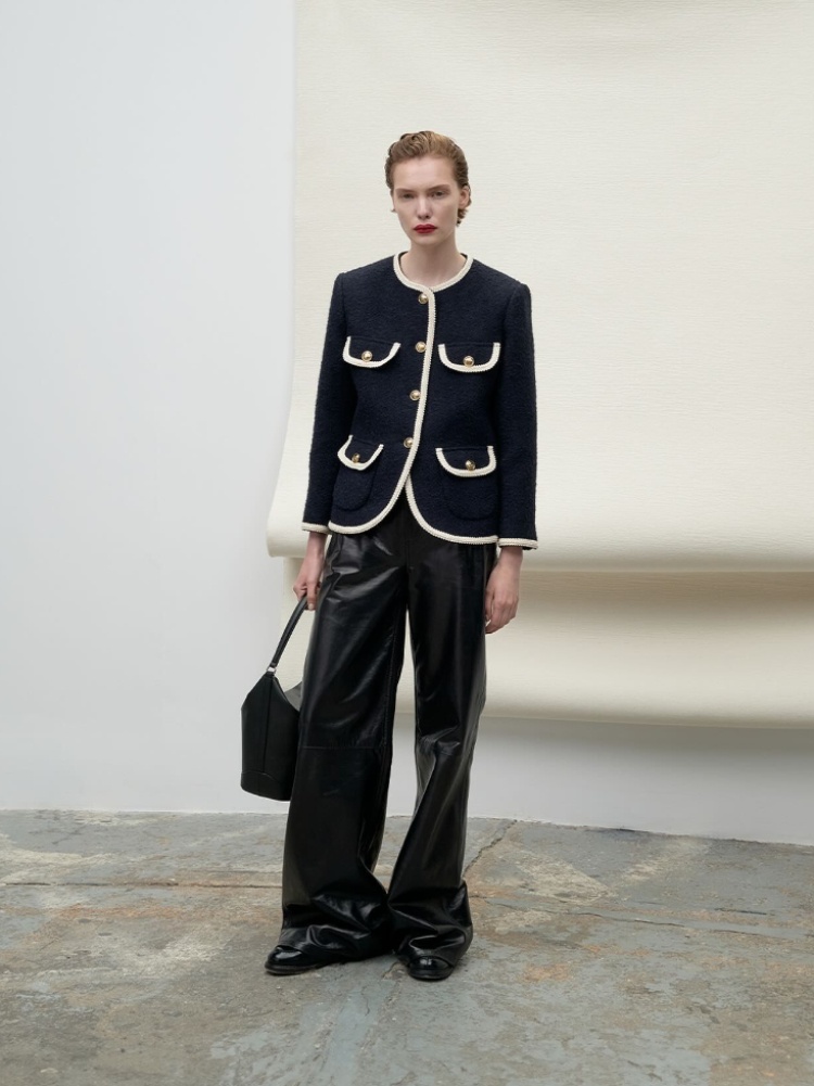 A Sandro model wearing a navy tweed jacket with gold buttons and leather pants