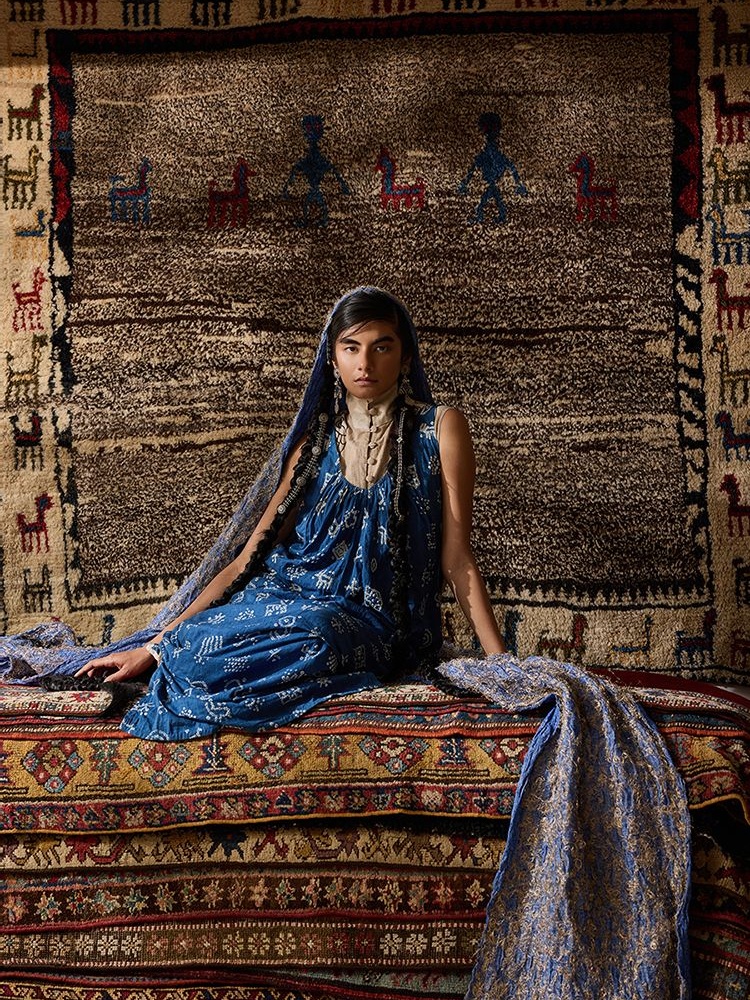 An early 20th-century Persian Gabbeh from the Zagros Mountains in ‘salt and pepper’ hues features human figures and animals . On Anika: 11.11/eleven eleven Indigo dress; Ka-Sha co-ord set; Akaaro stole; Pepper Coin jewellery